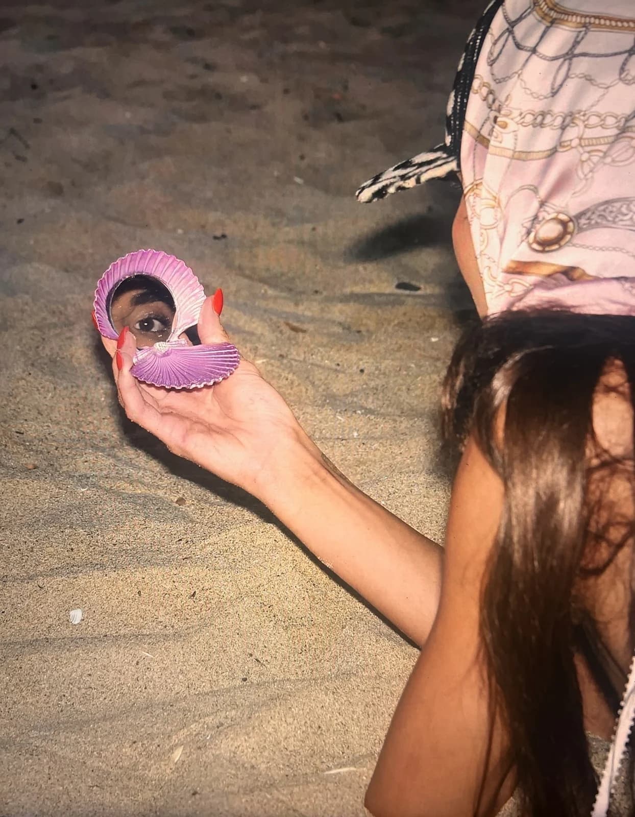 A purple shell mirror reflecting an eye on the beach