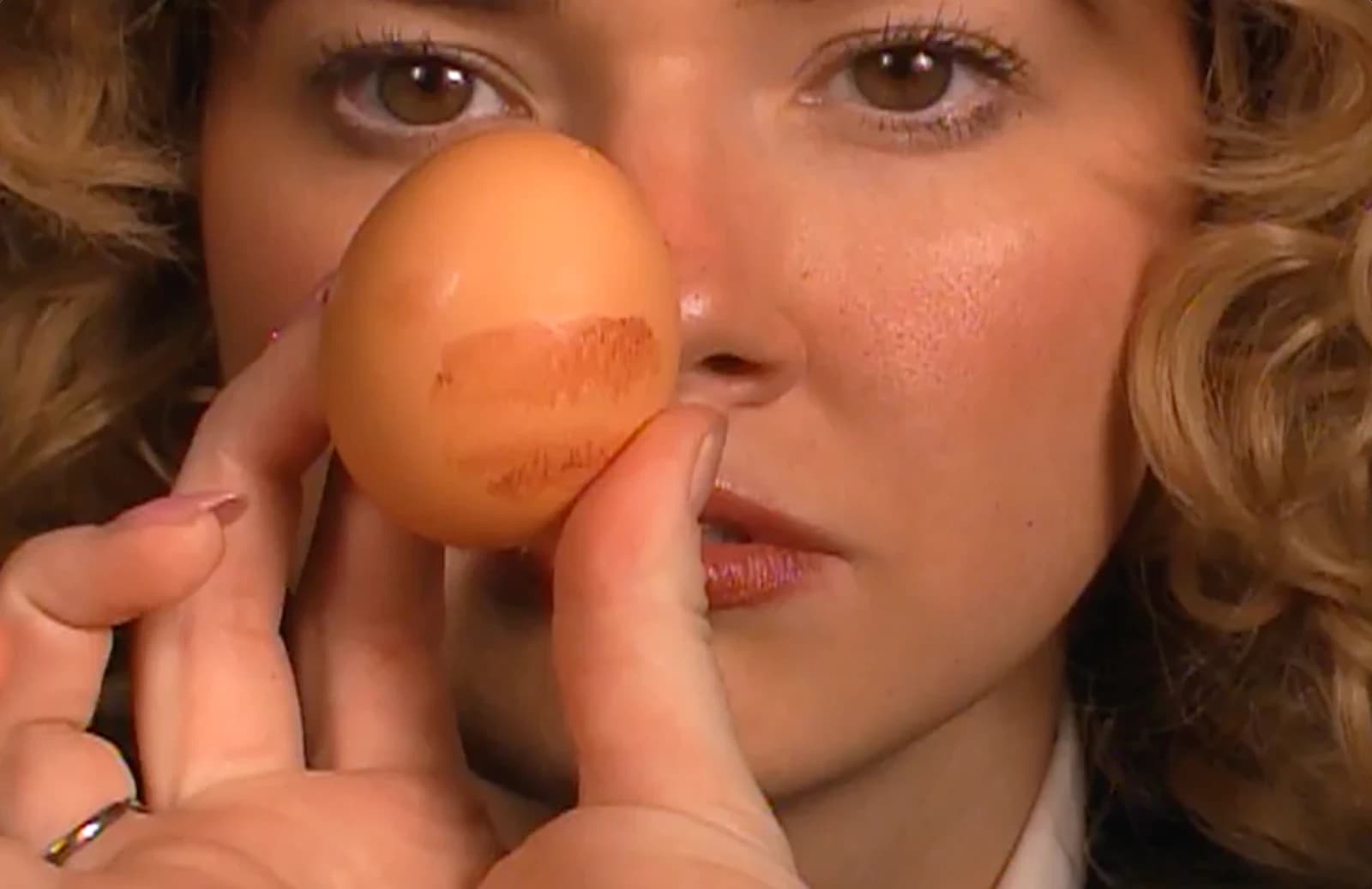 A news anchor holding a lipstick-marked egg beside her face