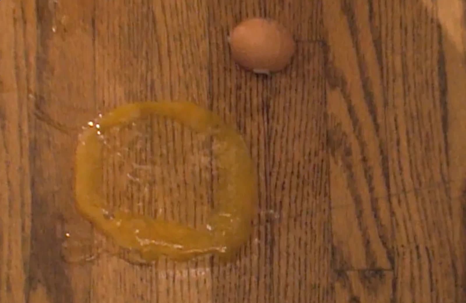 A cracked egg and yolk on the wooden floor