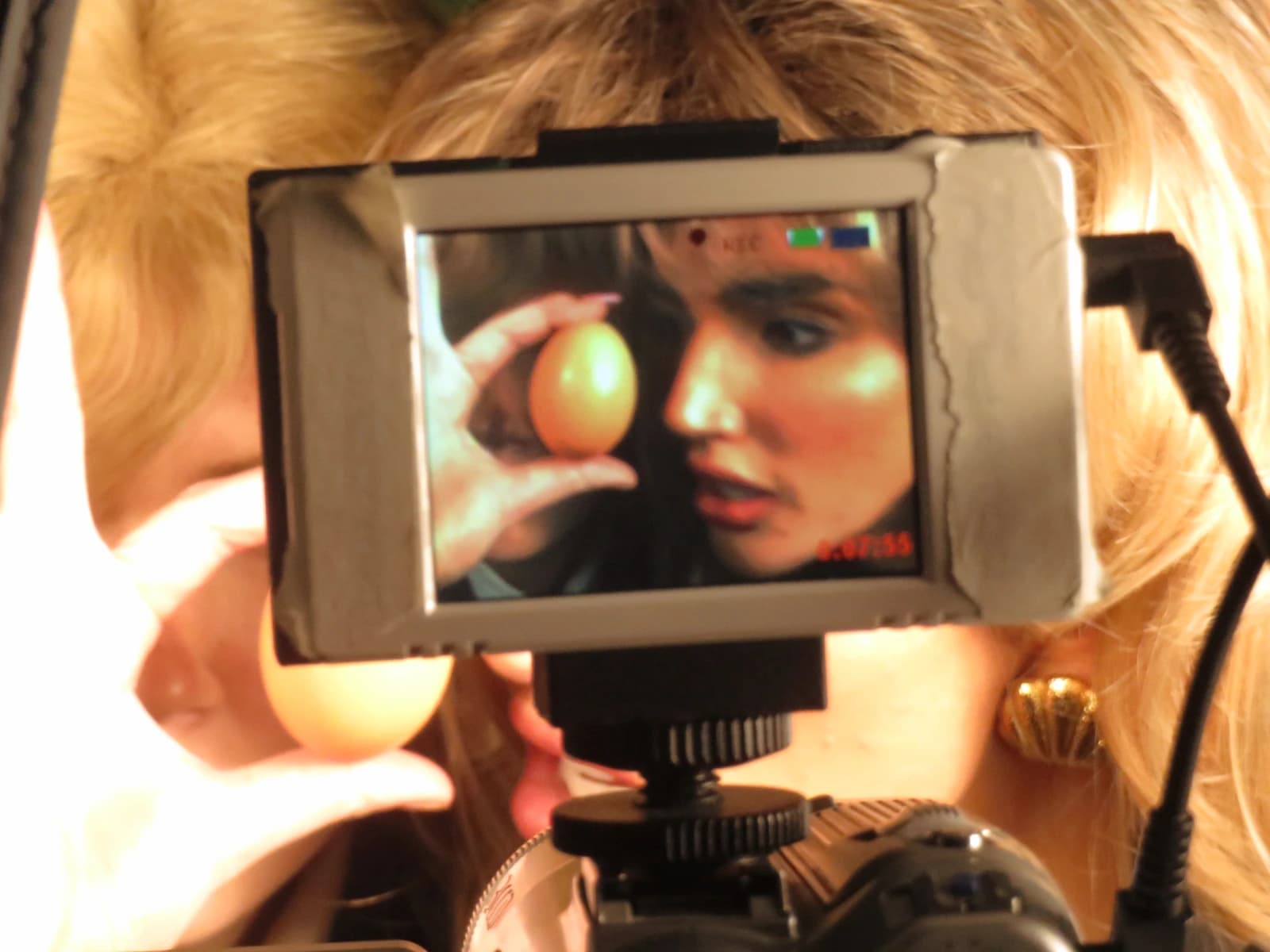 A news anchor holding an egg, seen through the on-set camera monitor